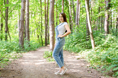 Portrait of woman walking on footpath amidst trees in forest
