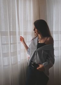 Woman looking away while standing against window at home