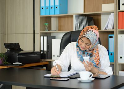 Midsection of woman holding coffee while sitting on table at home