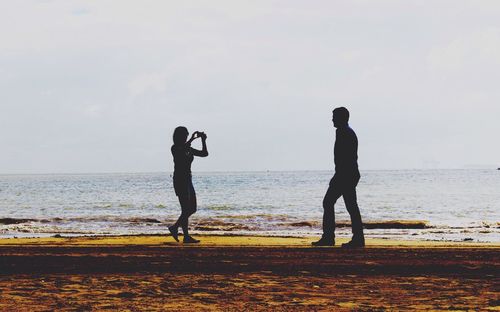 Silhouette people standing at beach against sky