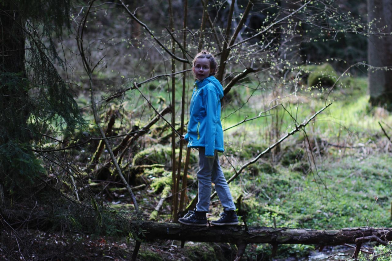 tree, forest, full length, tree trunk, standing, casual clothing, focus on foreground, lifestyles, nature, leisure activity, branch, outdoors, tranquility, front view, day, three quarter length, beauty in nature, rear view