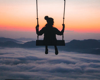 Low angle view of man swinging against sky during sunset
