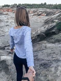 Rear view of woman holding boyfriend hand while standing on rock