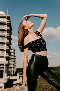 Midsection of woman with arms raised standing against sky