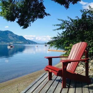 Empty chairs and table by lake against sky