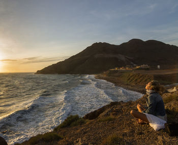 Woman sitting on beach by sea against sky