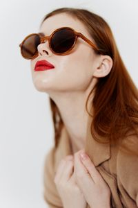 Close-up of young woman wearing sunglasses against white background