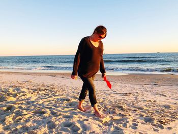 Full length of mature woman walking on sand at beach against sky during sunset