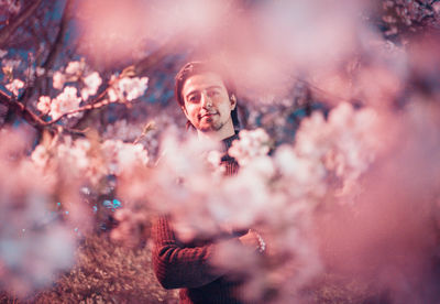 Portrait of confident young man with arms crossed standing by cherry tree at night