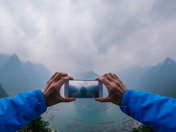 Close-up of man photographing against sky and mountains