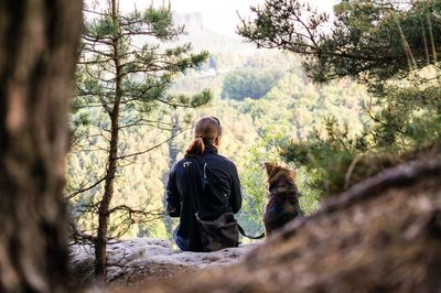 Rear view of woman with dog relaxing on cliff