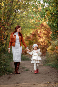 Mother and daughter walking on dirt road in forest
