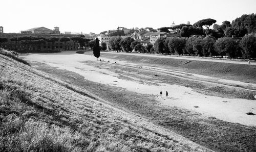 Field by old buildings in circus maximus against clear sky