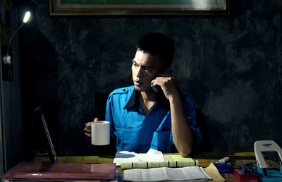 Businessman having coffee while talking on phone at desk