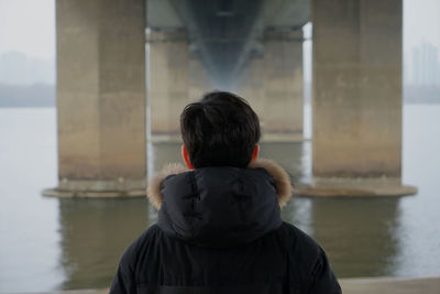 Rear view of man wearing warm clothing against bridge over river