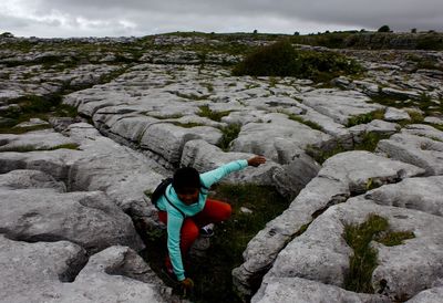 Boy crouching amidst rock formations at the burren