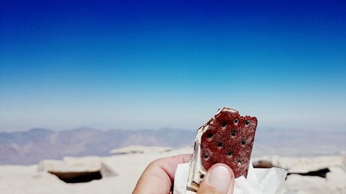 Cropped hand of person holding ice cream against sky