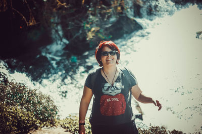 Young man wearing sunglasses standing against waterfall