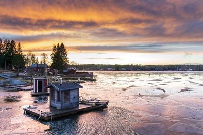 Floating huts on frozen lake against sky during sunset