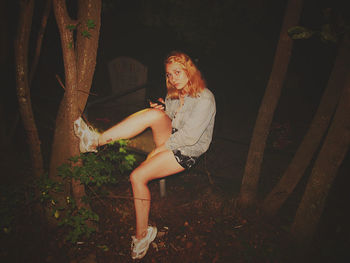 Portrait of woman sitting on railing at park during night