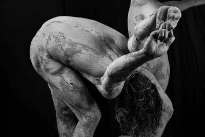 Naked man with mud on body against black background