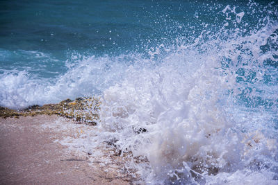 Wave crashing against exposed rock on beach creating a big splash