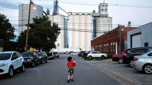 Rear view of boy running on street against factory in city