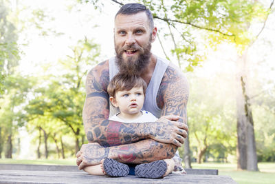 Portrait of smiling bearded man holding son sitting on bench