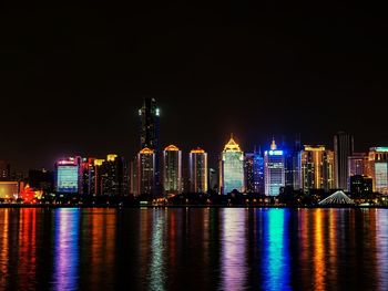 Illuminated cityscape by calm sea at night