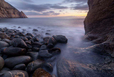 Rocks at sea shore against sky during sunset