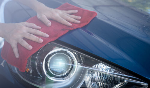 Car wash service. man hand holding red microfiber cloth and polish headlight of blue car. auto care