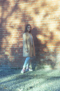 Full length of teenage girl standing against brick wall
