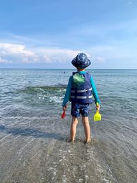 Rear view of man standing in sea against sky