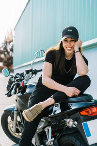 Positive female motorcyclist sitting on motorbike parked in city street on sunny day and looking at camera