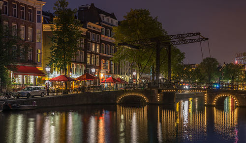 Illuminated bridge over river against buildings