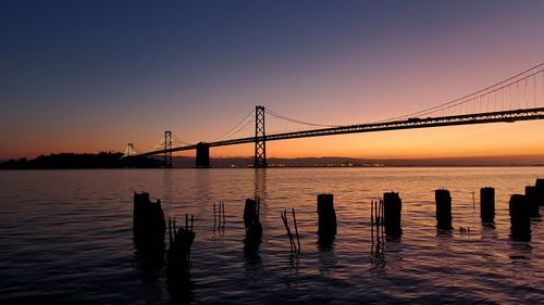 Silhouette bridge over sea against sky during sunset