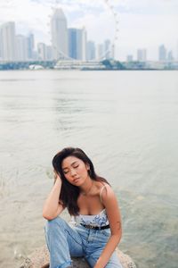 Beautiful young woman sitting or rock by sea