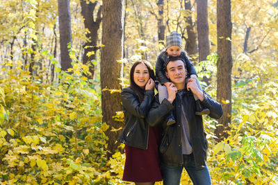 Portrait of smiling young woman standing against trees