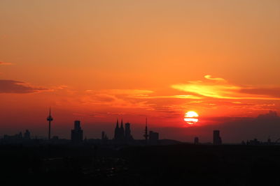 Silhouette of buildings against orange sky with sun