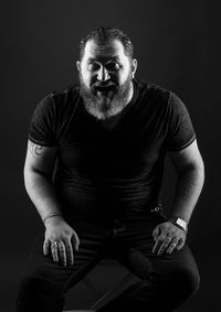 Portrait of man sitting against black background