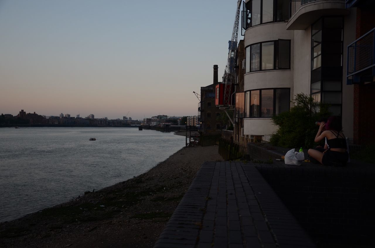 building exterior, architecture, built structure, clear sky, water, city, copy space, sky, sunset, sea, sunlight, outdoors, transportation, incidental people, river, city life, men, railing, shadow