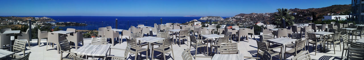 Panorama view of wooden tables and chairs of a greek tavern at daytime and the view of beach. greece