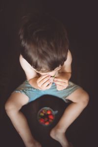 High angle view of shirtless boy eating fruit against black background