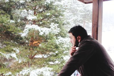 Young man looking away while standing by railing