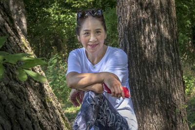 Portrait of smiling senior woman sitting against tree in forest