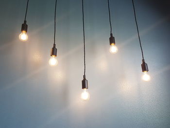 Low angle view of illuminated light bulbs hanging against wall