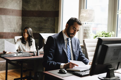 Confident male lawyer reading diary with female colleague working in background at office