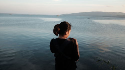 Rear view of woman standing at beach against sky