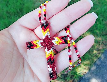 Cropped hand holding religious cross of beads outdoors