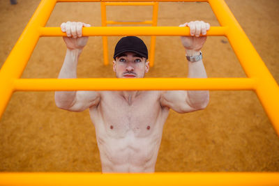 Man with cap doing pull-ups in a calisthenics park. high angle
